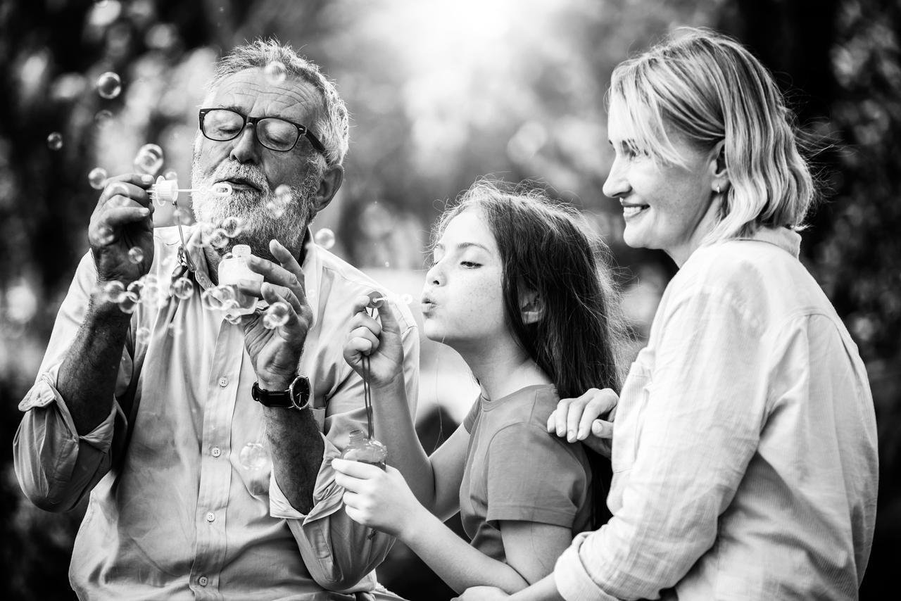 A grandfather, mother and daughter blowing bubbles together outdoors
